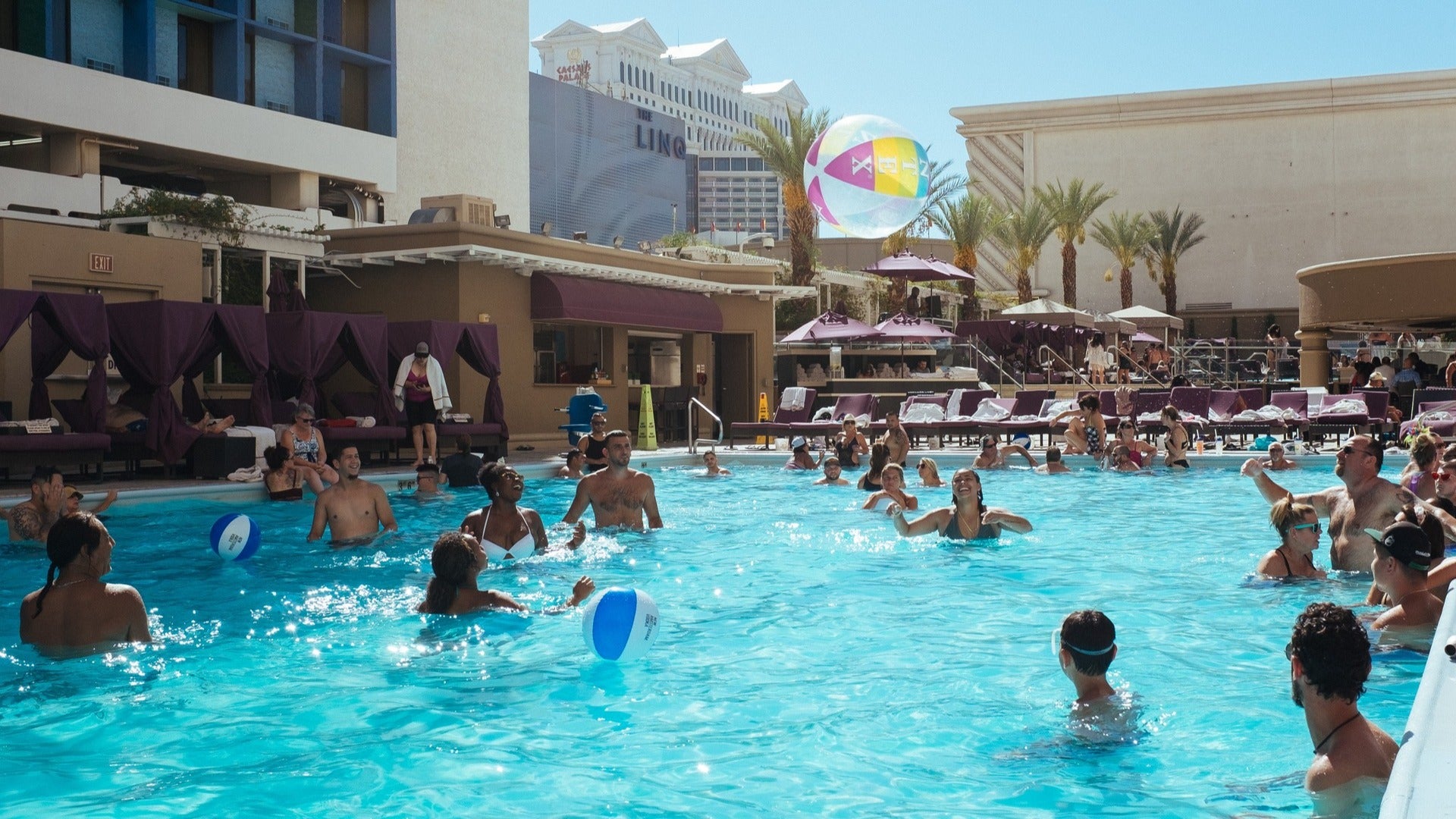 hotel pool with people swimming and enjoying, pool cabanas and chairs on the side
